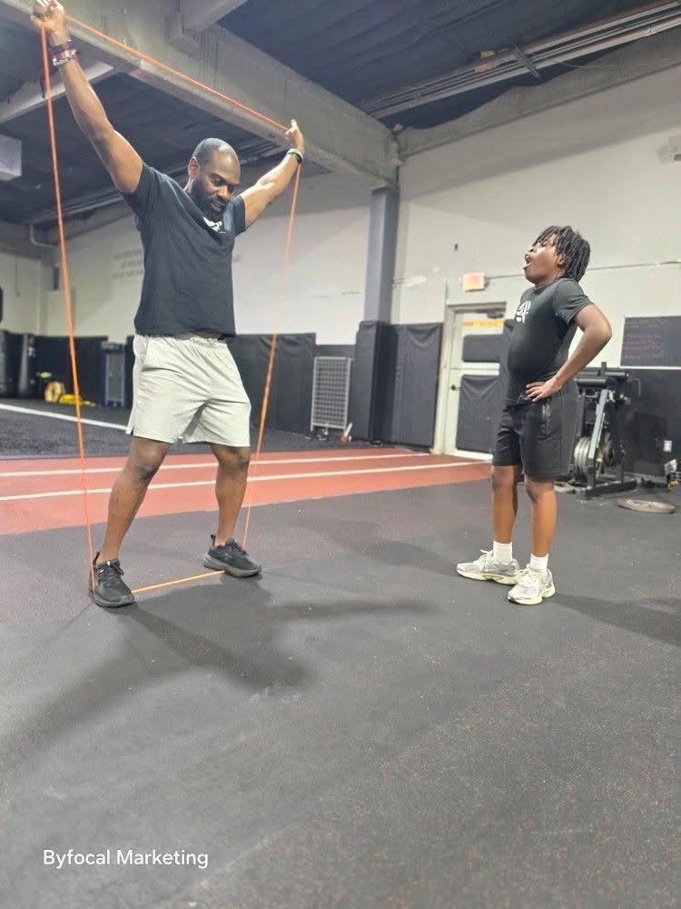 Coach demonstrating a resistance-band movement to a young athlete